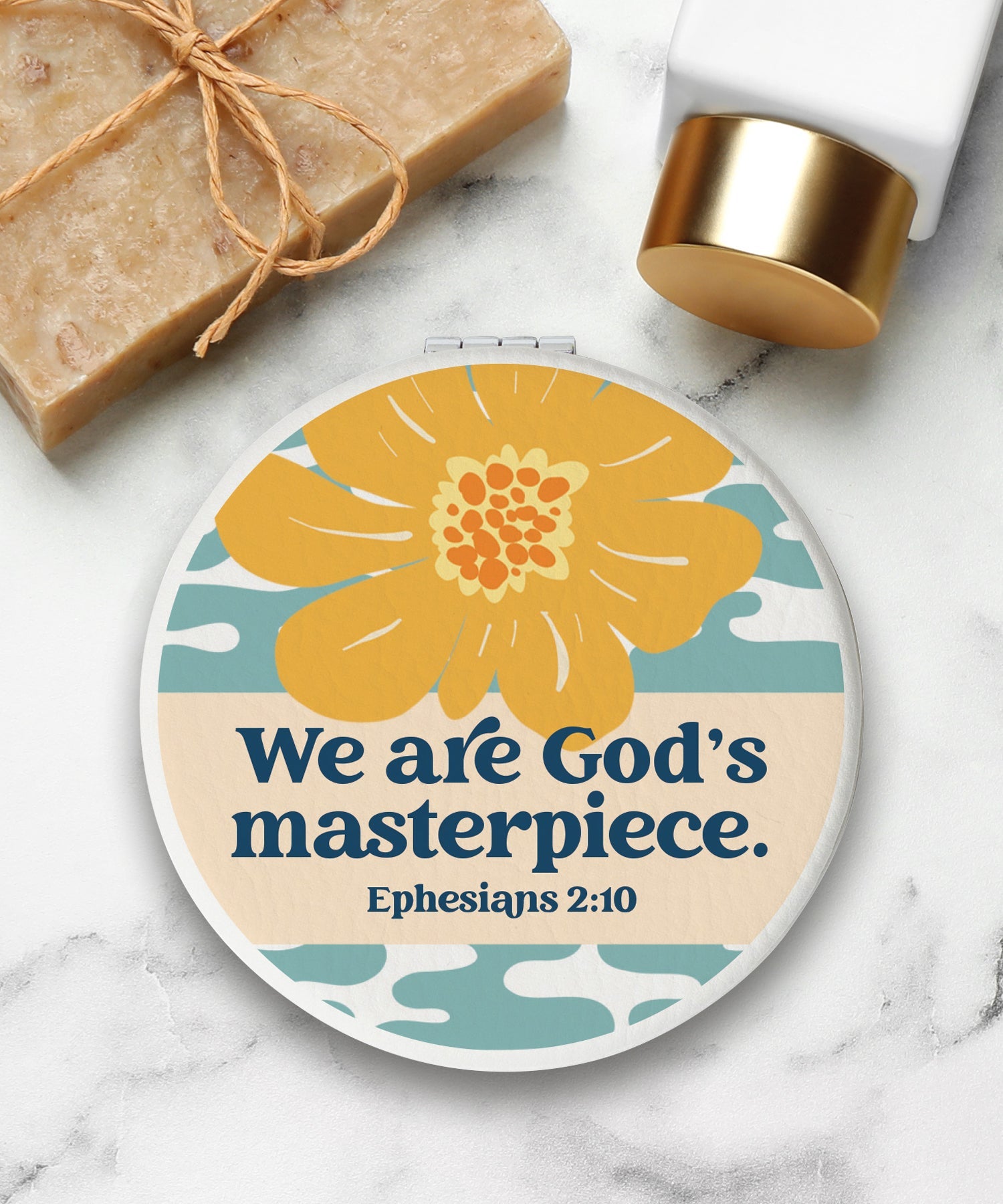 Round compact mirror with a leatherette cover, full-color “We are God’s Masterpiece” design, 1X and 2X mirrors inside, and magnetic closure.