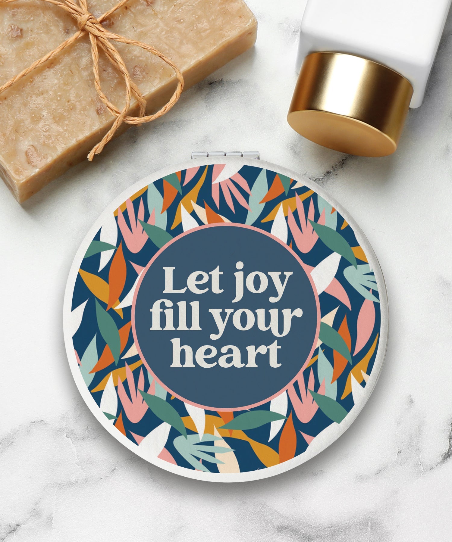 Round compact mirror with a leatherette cover, full-color “Let Joy Fill Your Heart” design, 1X and 2X mirrors inside, and magnetic closure.