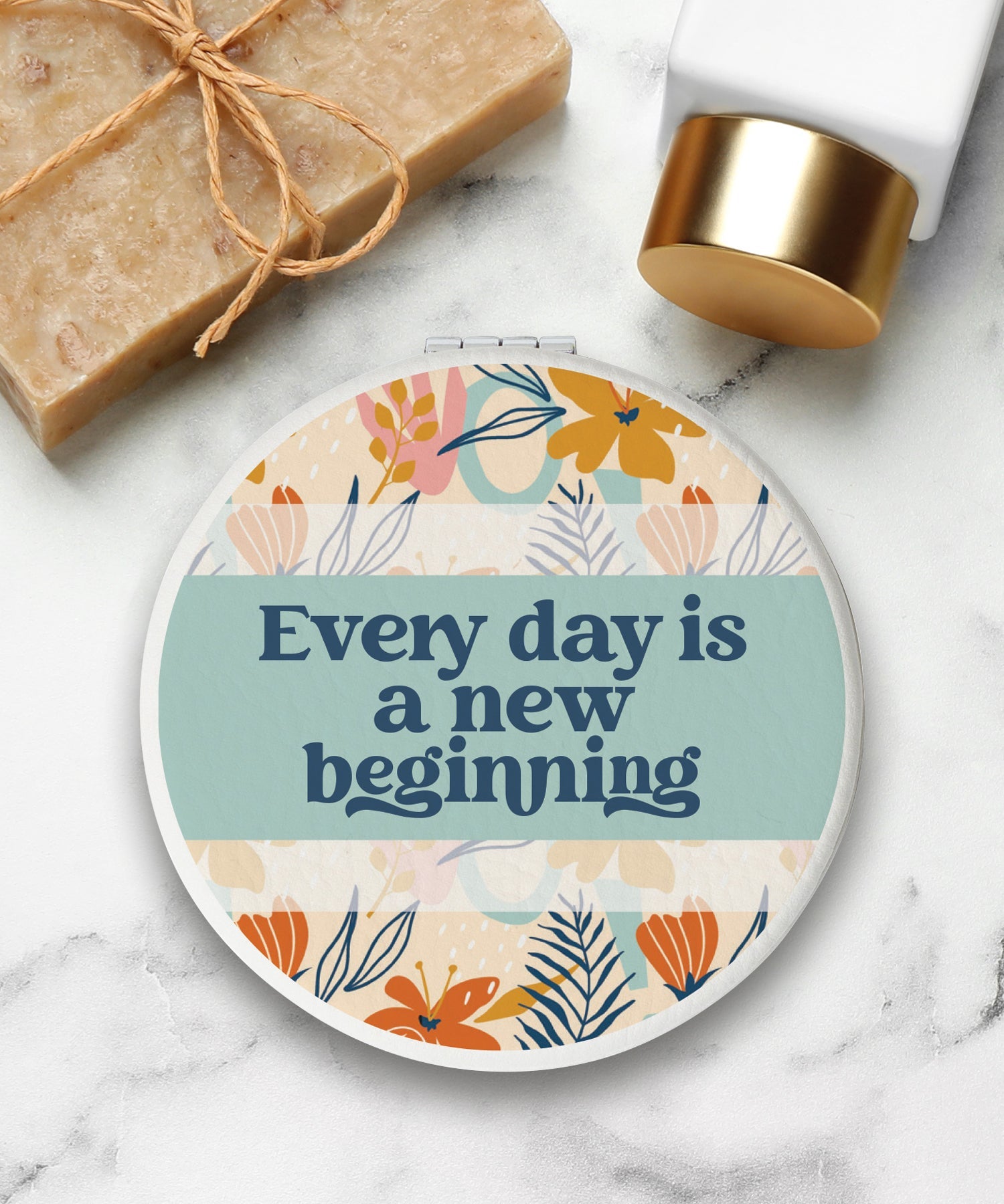 Round compact mirror with a leatherette cover, full-color “Every Day Is a New Beginning” design, 1X and 2X mirrors inside, and magnetic closure.