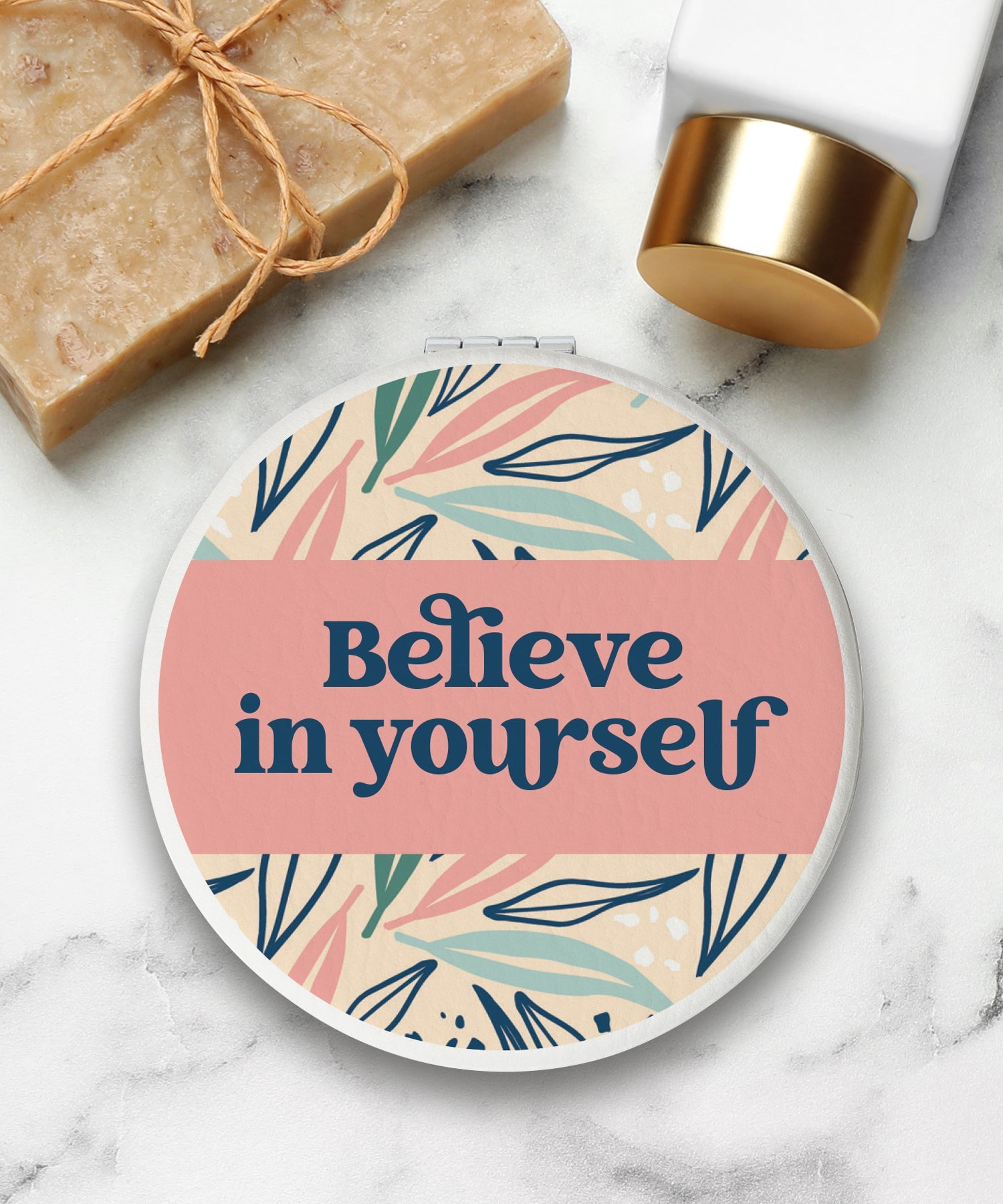 Round compact mirror with a leatherette cover, full-color “Believe in Yourself” design, 1X and 2X mirrors inside, and magnetic closure.