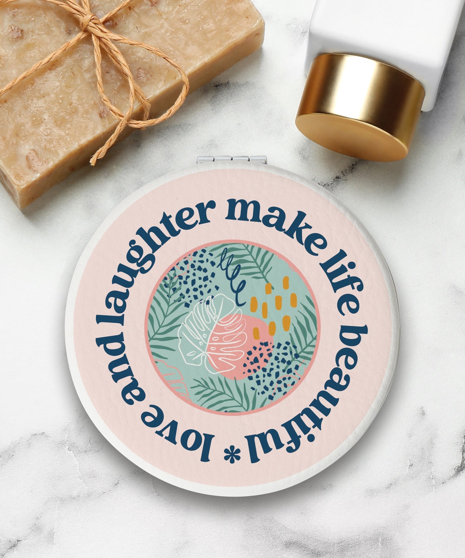 Round compact mirror with a leatherette cover, full-color “Love and Laughter” design, 1X and 2X mirrors inside, and magnetic closure.