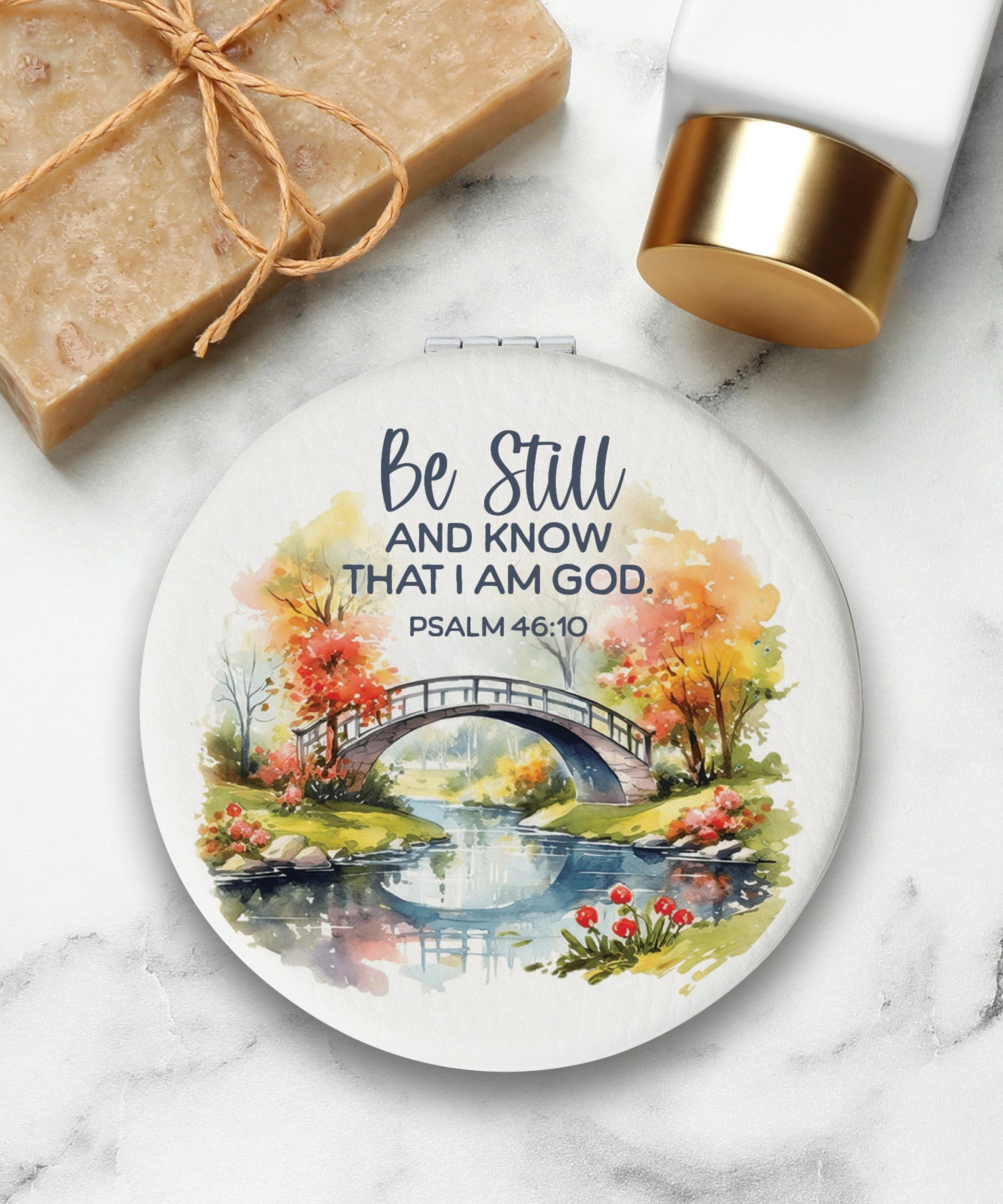 Round compact mirror with a leatherette cover, full-color “Be Still and Know” design, 1X and 2X mirrors inside, and magnetic closure.