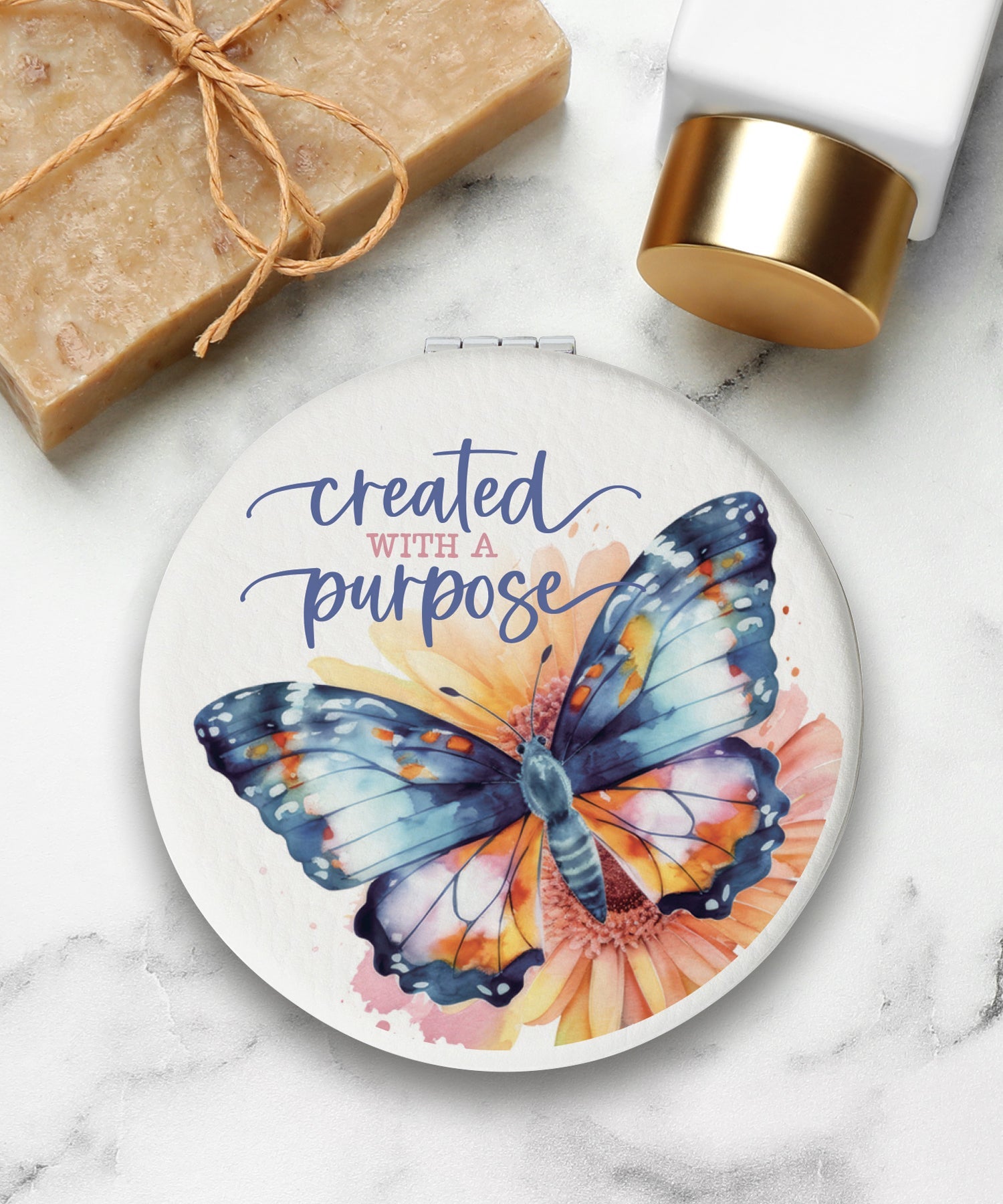 Round compact mirror with a leatherette cover, full-color “Created With a Purpose” design, 1X and 2X mirrors inside, and magnetic closure.